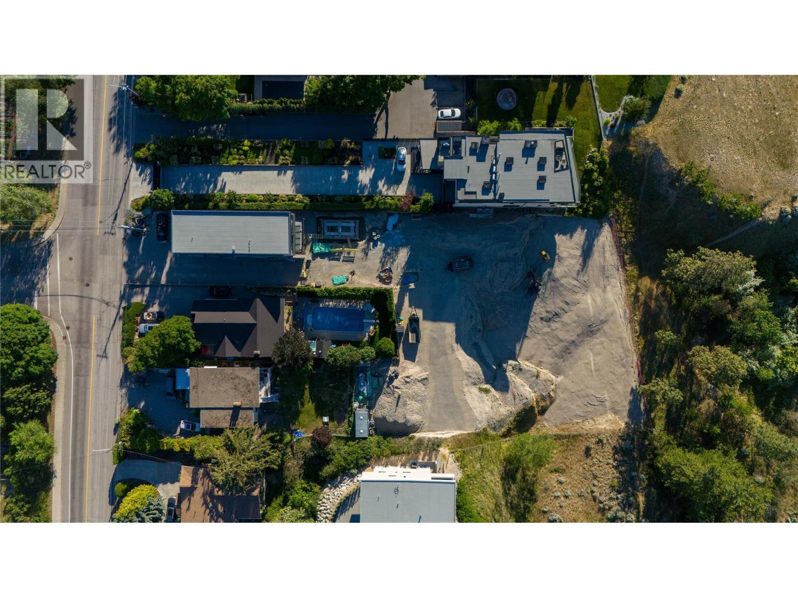 Aerial view of a cleared construction site beside a road and neighboring homes.