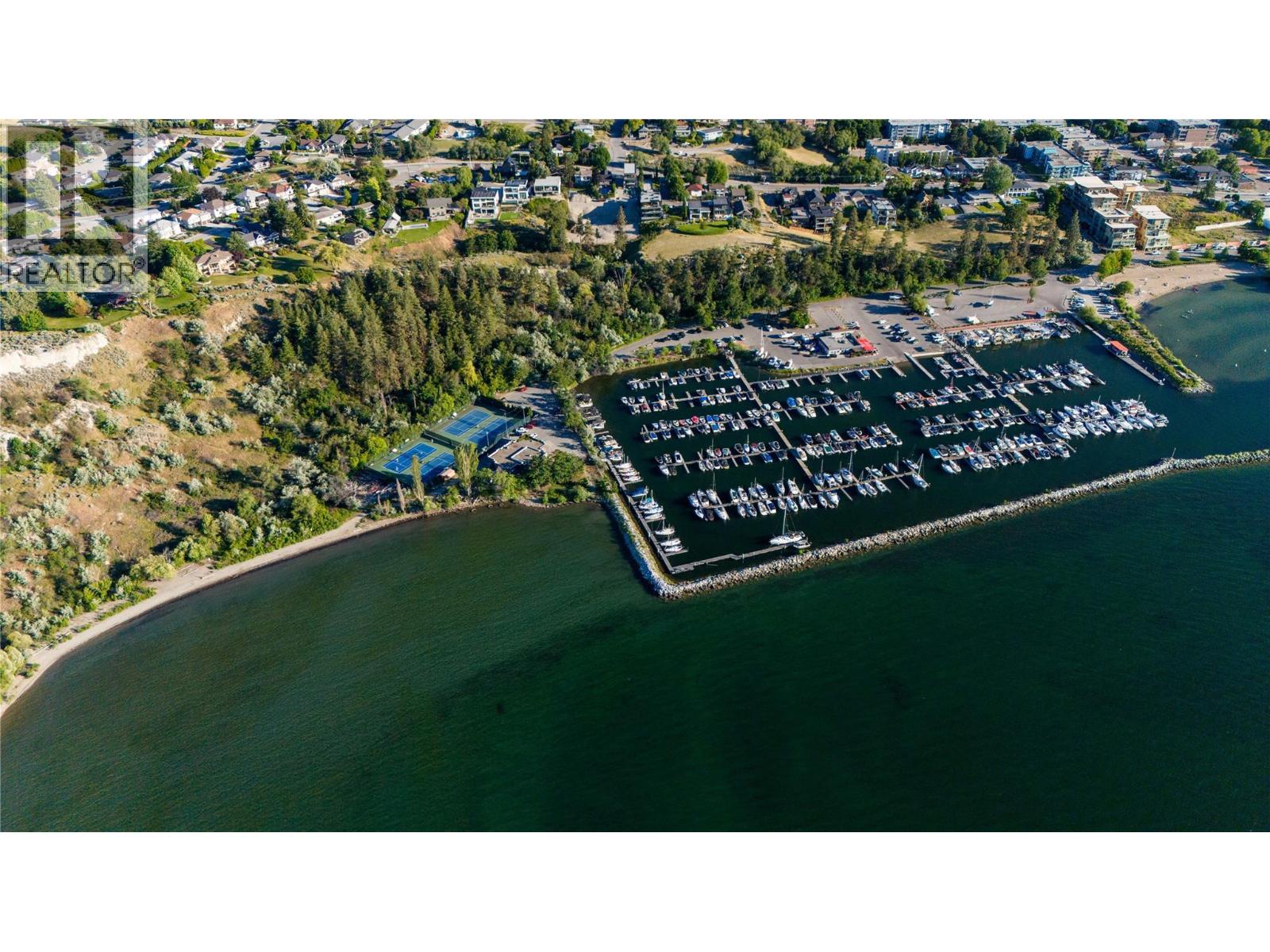 Aerial view of a waterfront marina with rows of boats, shoreline homes, and tennis courts.