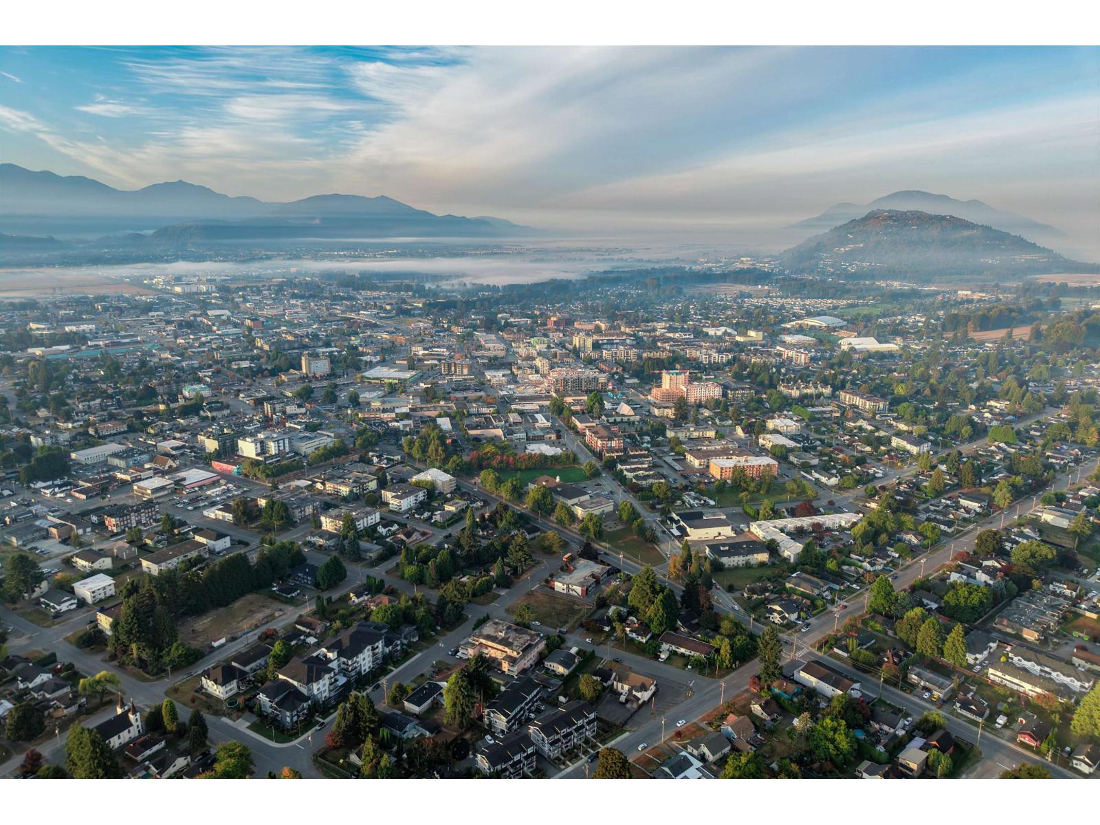 Aerial view of Chilliwack with residential neighborhoods, commercial buildings, and misty mountains.