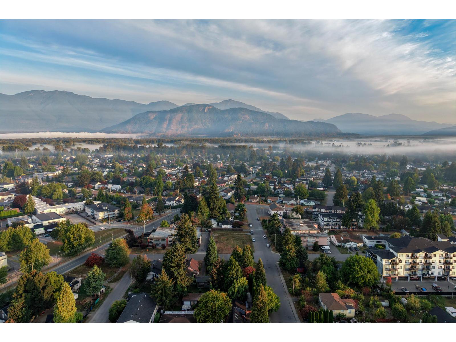 Aerial view of a Chilliwack neighborhood, misty valley, and surrounding mountains.