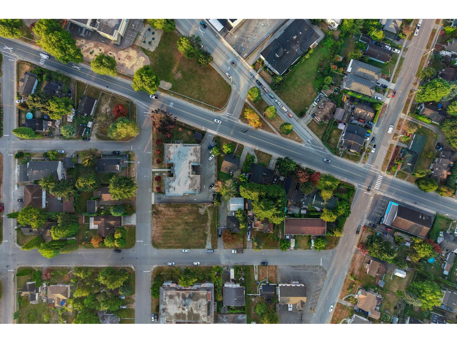 Aerial view of a Chilliwack neighborhood with tree-lined streets, homes, commercial buildings, and vacant lots.