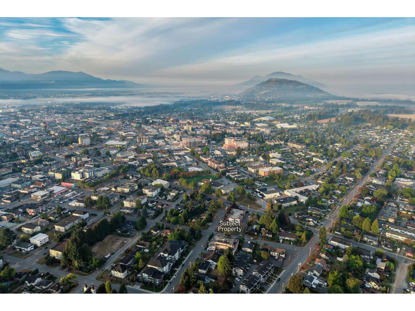 Aerial view of Chilliwack neighborhoods and commercial buildings, with mist and mountains in the distance.