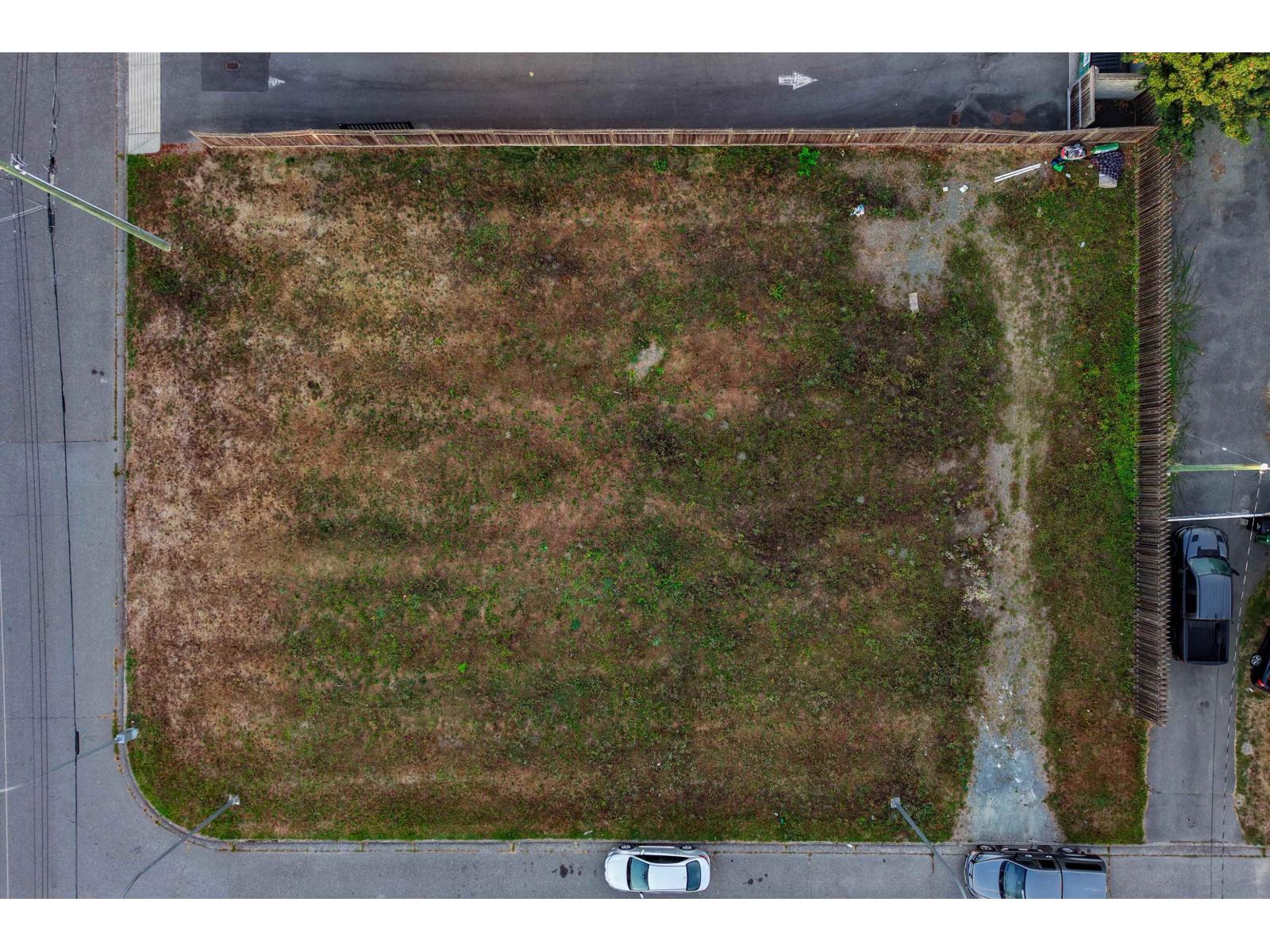 Aerial view of a vacant grassy lot bordered by streets and wooden fencing.