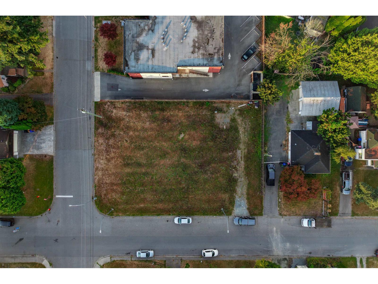 Aerial view of a vacant corner lot bordered by roads, homes, and a commercial building.