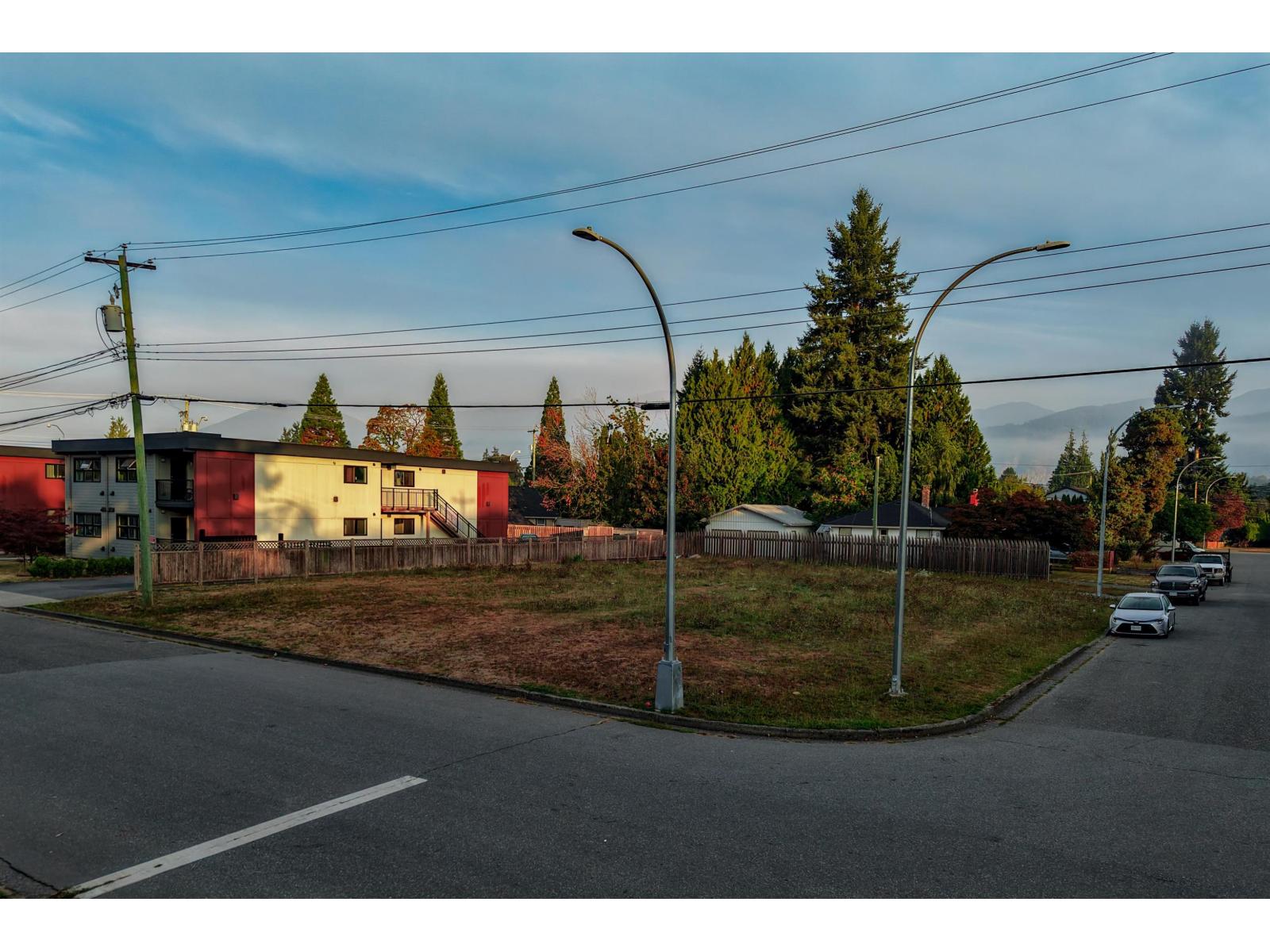 Vacant corner lot with sparse grass, a wooden fence, and streets on two sides.