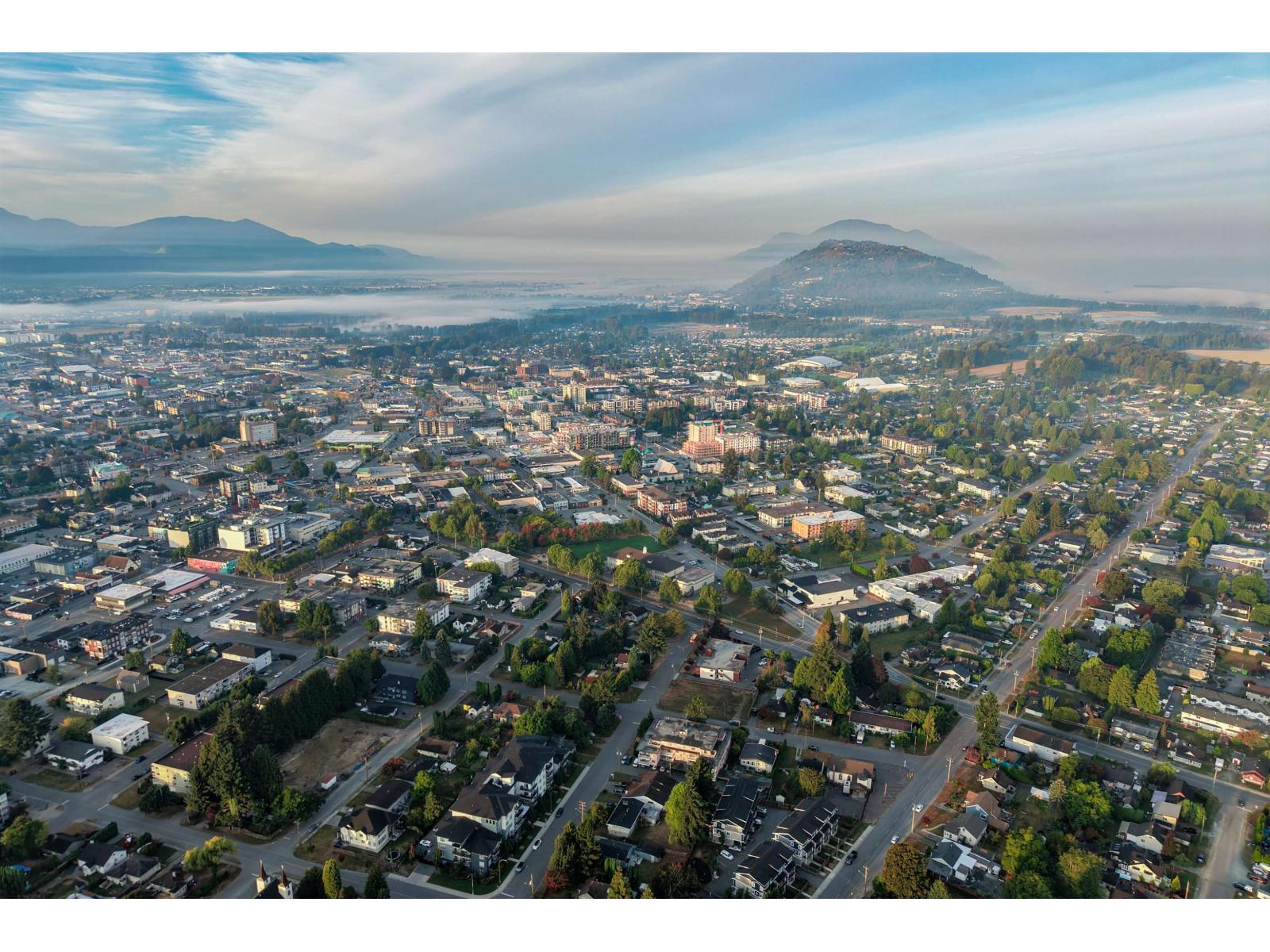 Aerial view of Chilliwack with neighborhoods, valley clouds, and mountains in the distance.