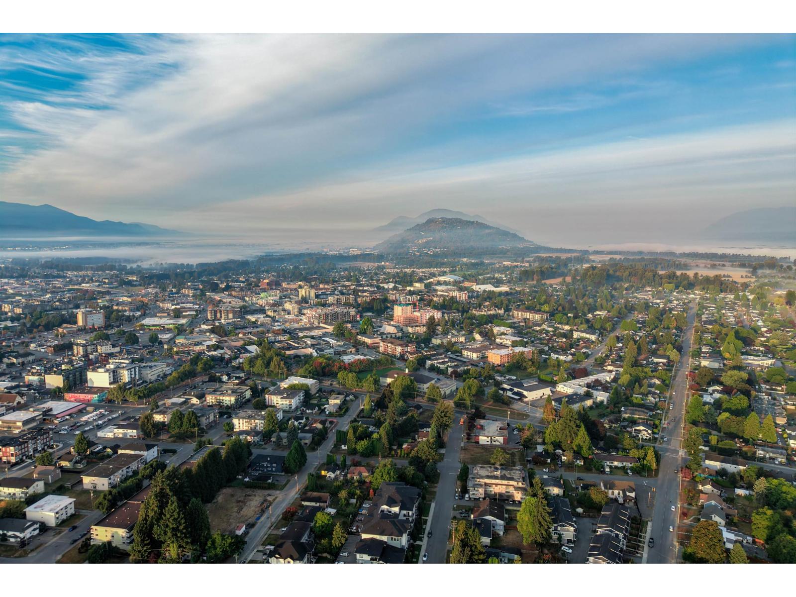 Aerial view of Chilliwack neighborhoods beneath a prominent hill and misty mountains.