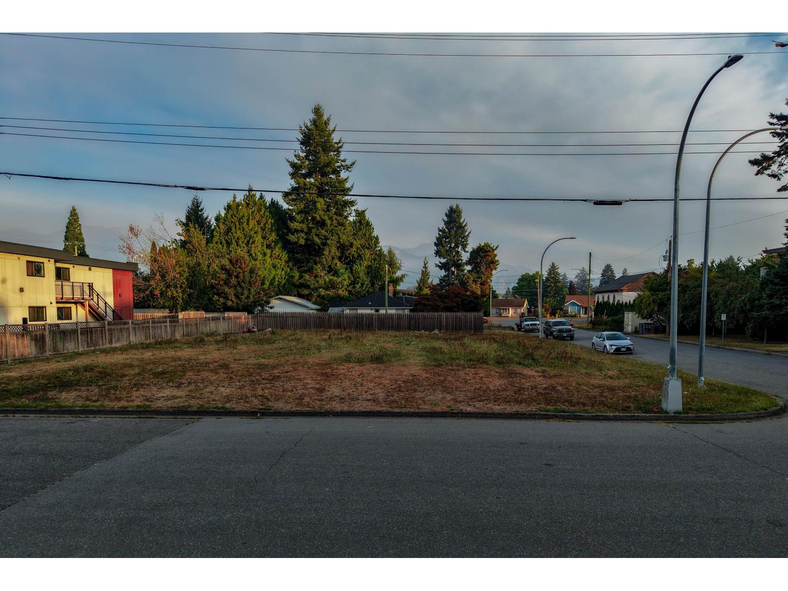 Vacant lot with patchy grass, neighboring homes, overhead wires, and distant mountains.