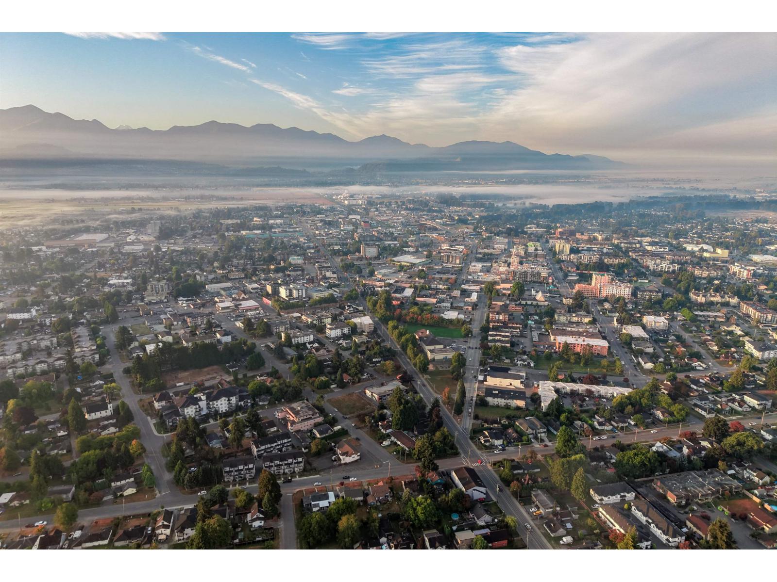 Aerial view of Chilliwack’s neighborhoods and city center, with fog across the valley and mountains beyond.