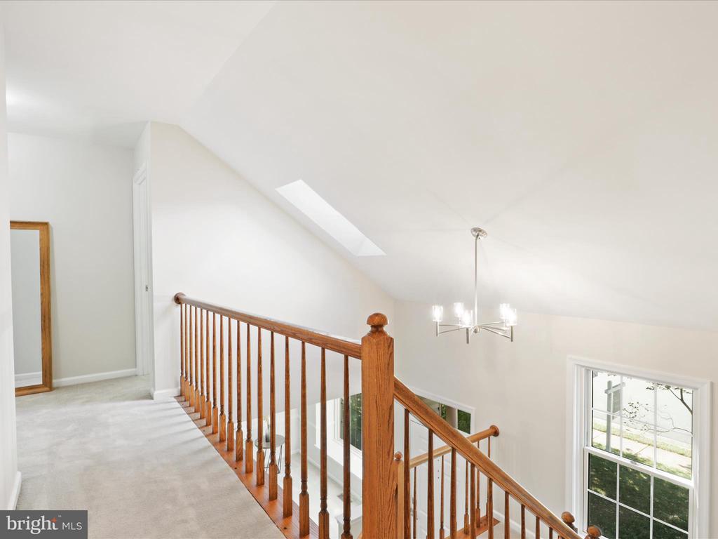 Upstairs landing with a skylight, wood staircase railing, chandelier, and large window.