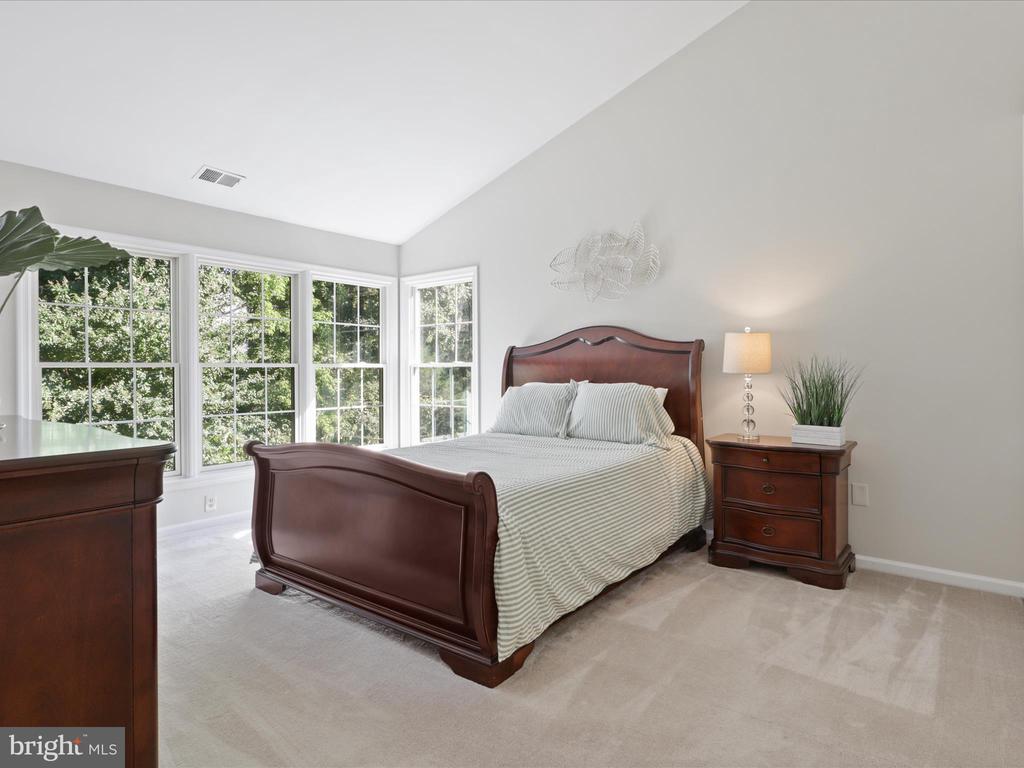 Bedroom with a dark wood bed, striped bedding, beige carpet, and tall windows overlooking trees.