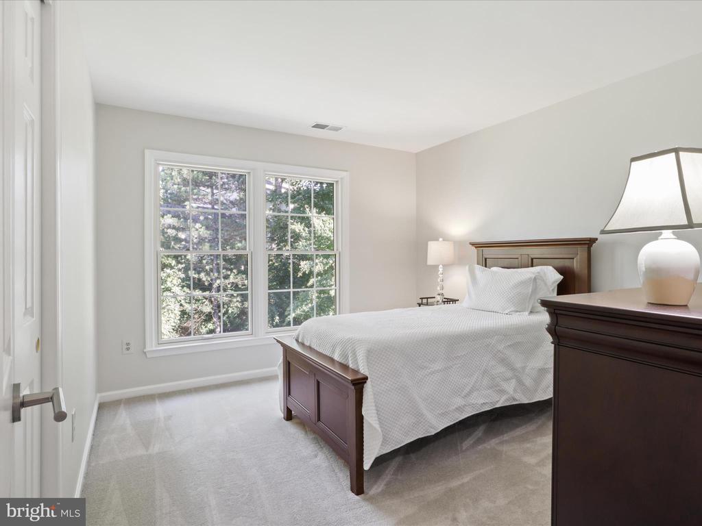 Furnished bedroom with a dark wood bed, white bedding, and large windows overlooking trees.
