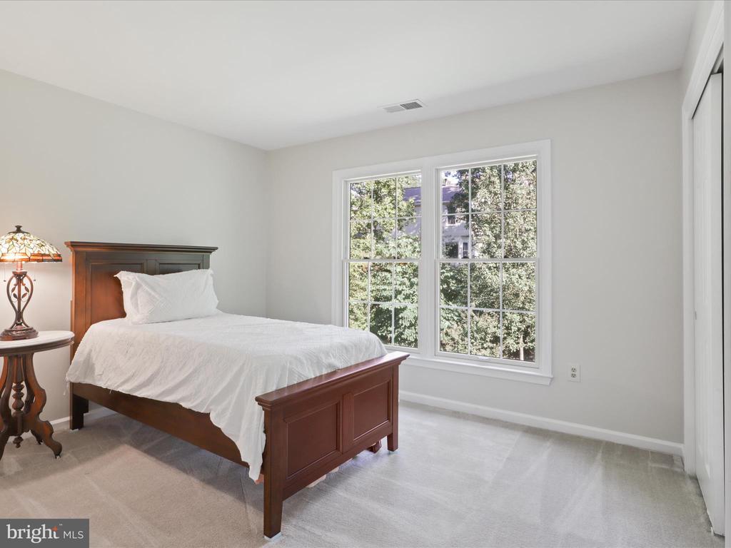Bedroom with a dark wood bed, white bedding, and a large window overlooking leafy trees.