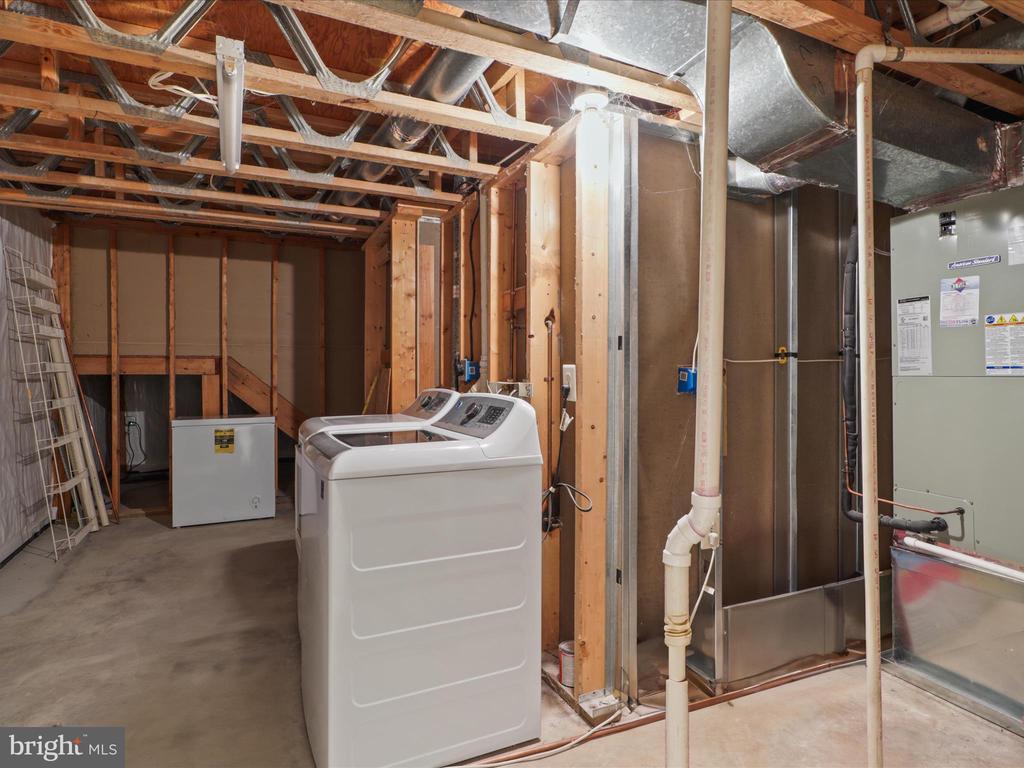Basement laundry and utility area with washer, dryer, exposed framing, and HVAC equipment.