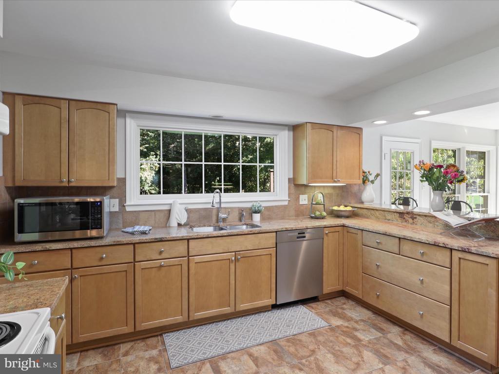 Kitchen with honey-toned cabinets, stone counters, and a large window overlooking trees.