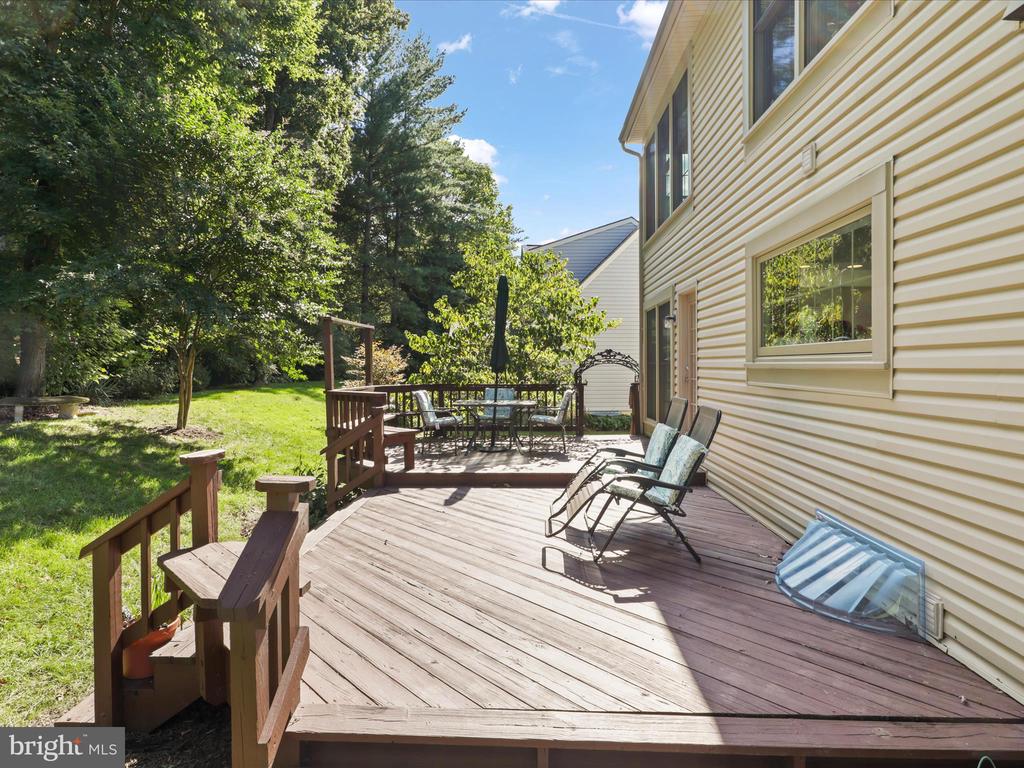 Backyard wooden deck with outdoor seating beside a light-sided house and tree-lined lawn.