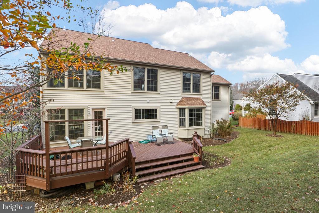 Rear of a beige two-story house with a raised wooden deck, patio furniture, and a broad lawn.