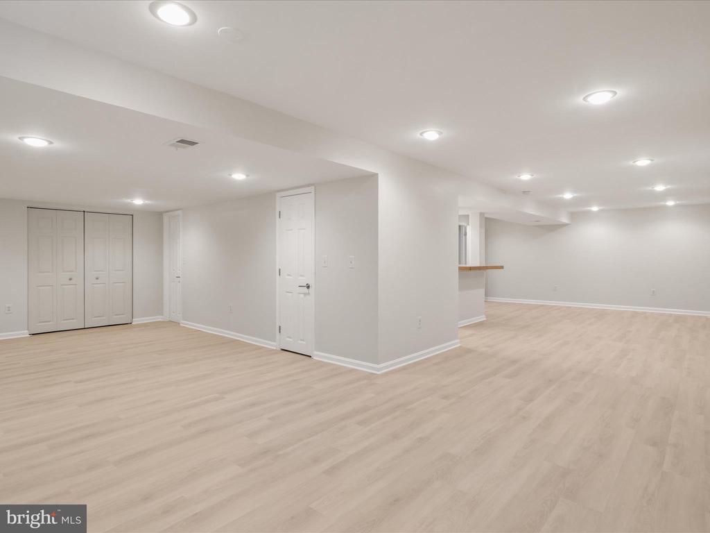 Vacant finished room with light wood-look flooring, recessed lights, closet doors, and a wood-topped counter.