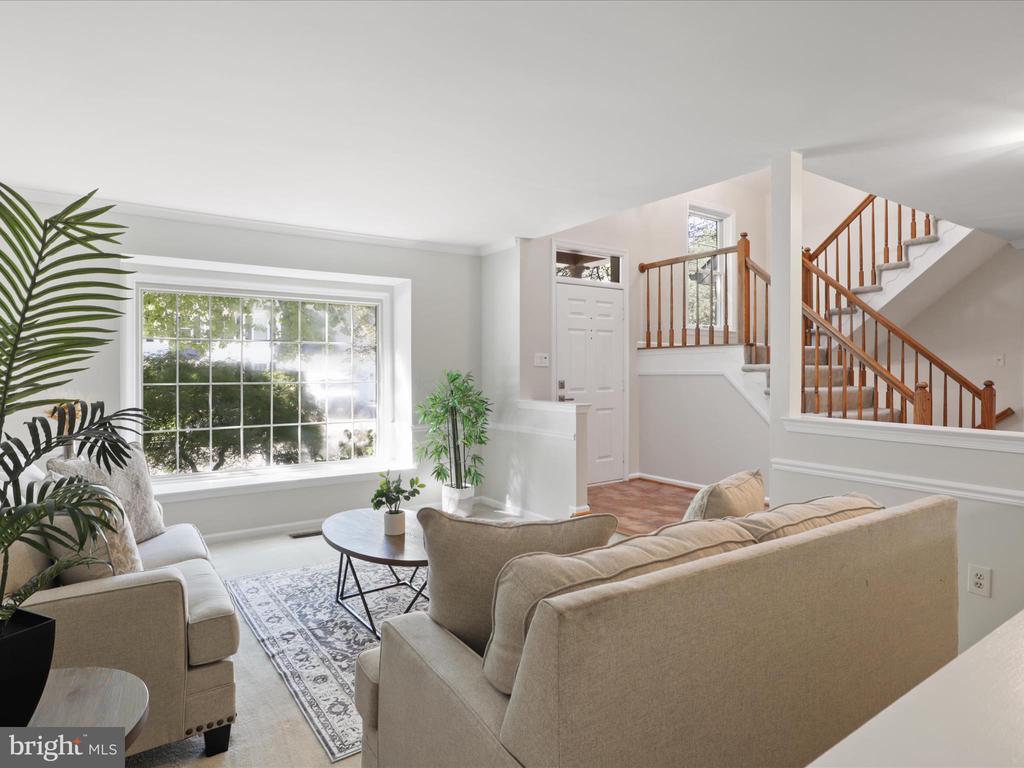 Furnished living room with neutral sofas, a large window, and a wooden-railed staircase.