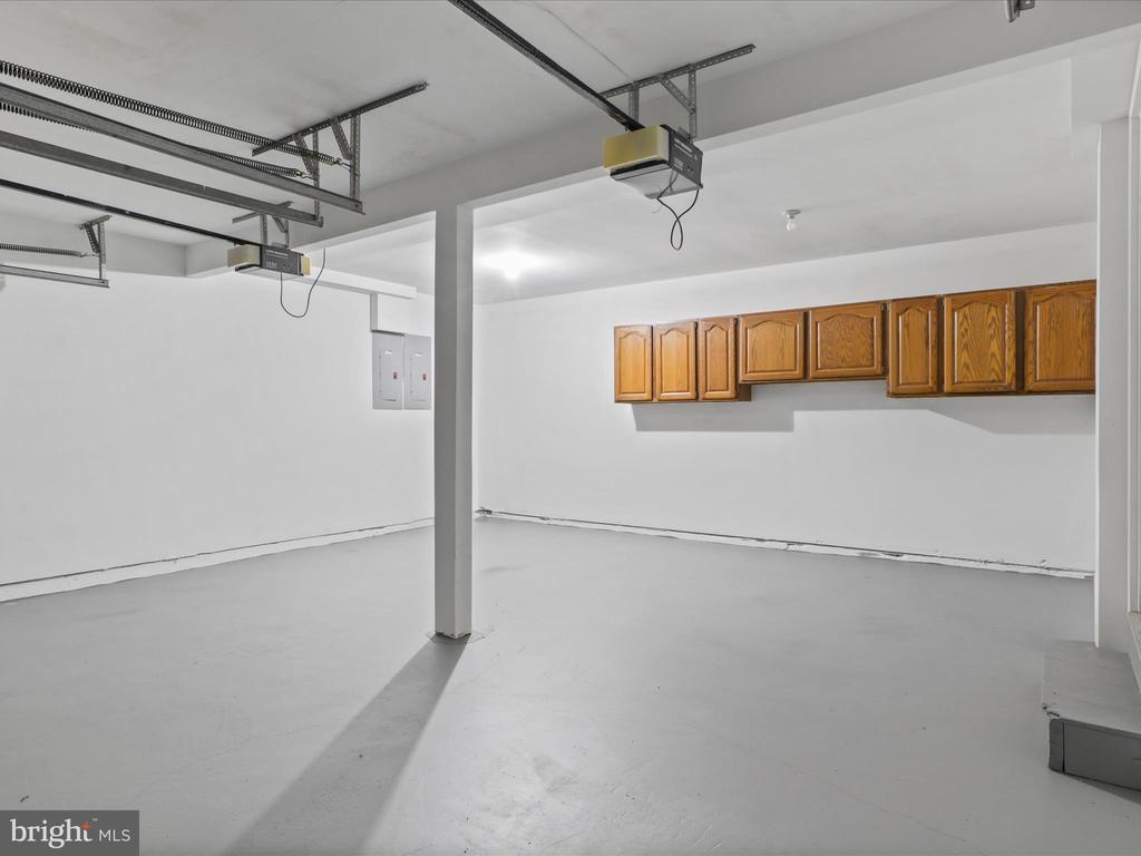 Empty garage with overhead door tracks, a support column, and wall-mounted wooden cabinets.