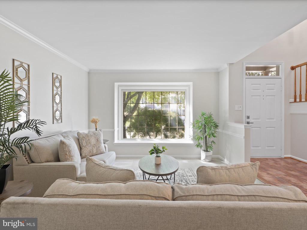 Furnished living room with neutral sofas, a large grid-pane window, and leafy trees outside.