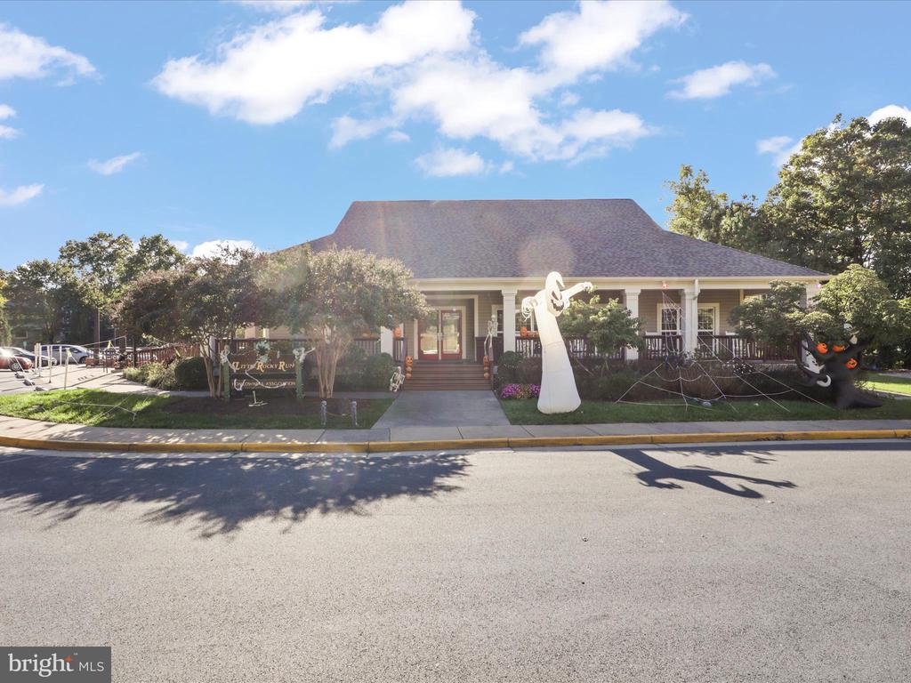 Low building with a covered, columned porch, landscaped front yard, and Halloween decorations.