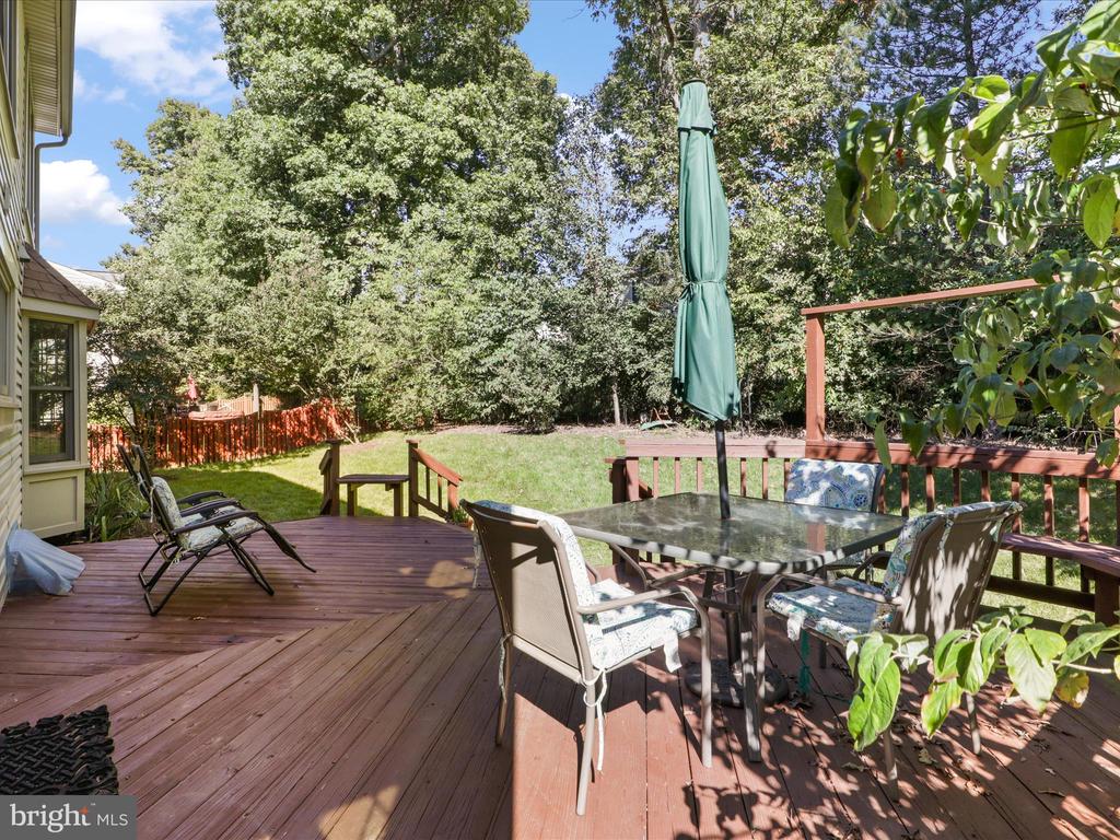 Wood deck with outdoor dining set and closed umbrella overlooking a leafy backyard.
