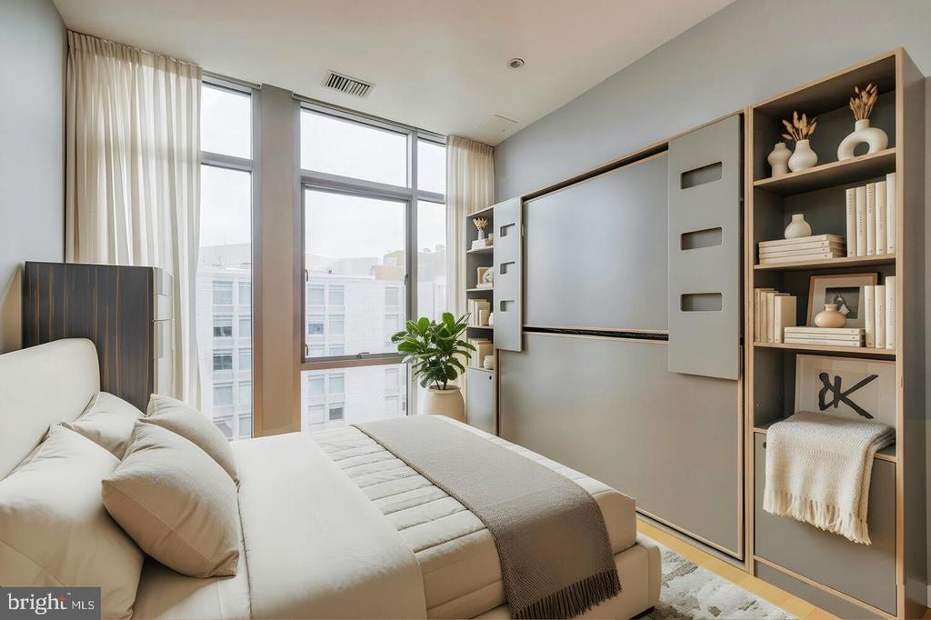Staged bedroom with a white upholstered bed, tall windows, and built-in shelving.