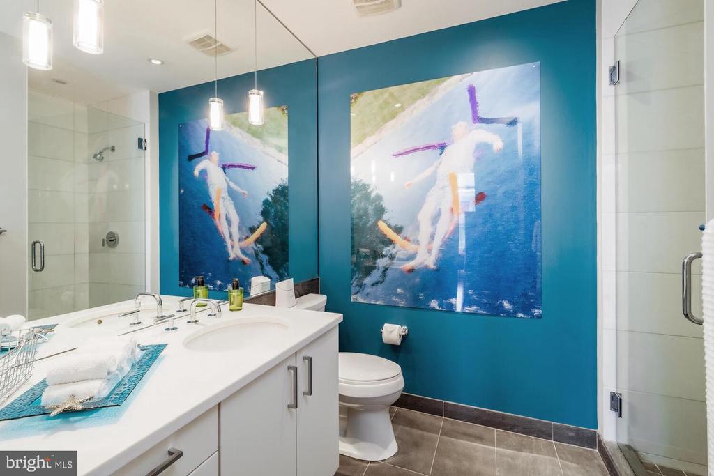 Bathroom with a white vanity, glass shower enclosures, and colorful artwork on a teal wall.