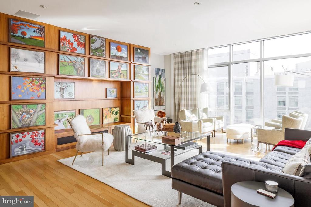 Living room with floor-to-ceiling windows, a leather sectional, and built-in shelving filled with framed artwork.