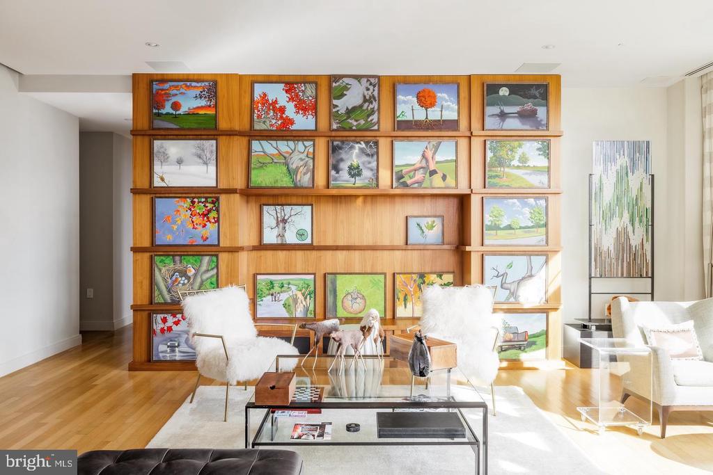 Living room with a large wood display wall of framed artwork and white lounge chairs.