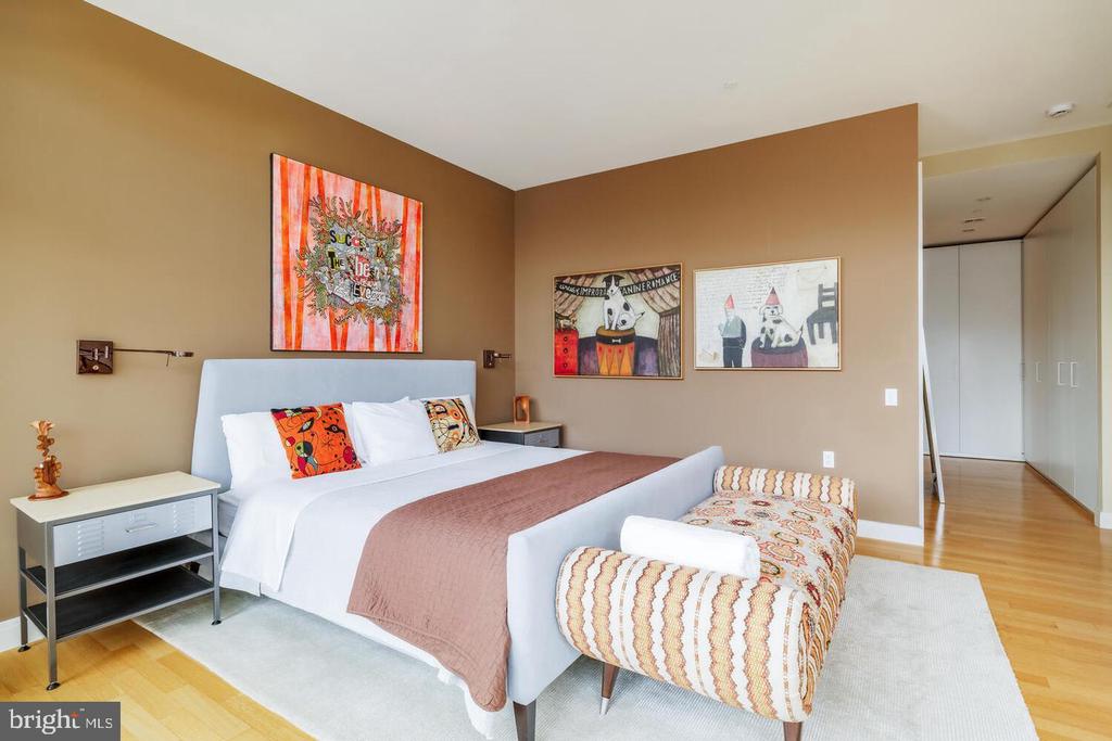 Furnished bedroom with a white bed, colorful pillows, patterned bench, and warm tan walls.