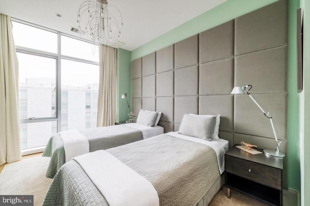 Staged bedroom with two twin beds, a floor-to-ceiling padded headboard, and large windows.