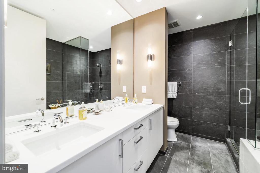 Modern bathroom with a double vanity and glass shower against dark tile.