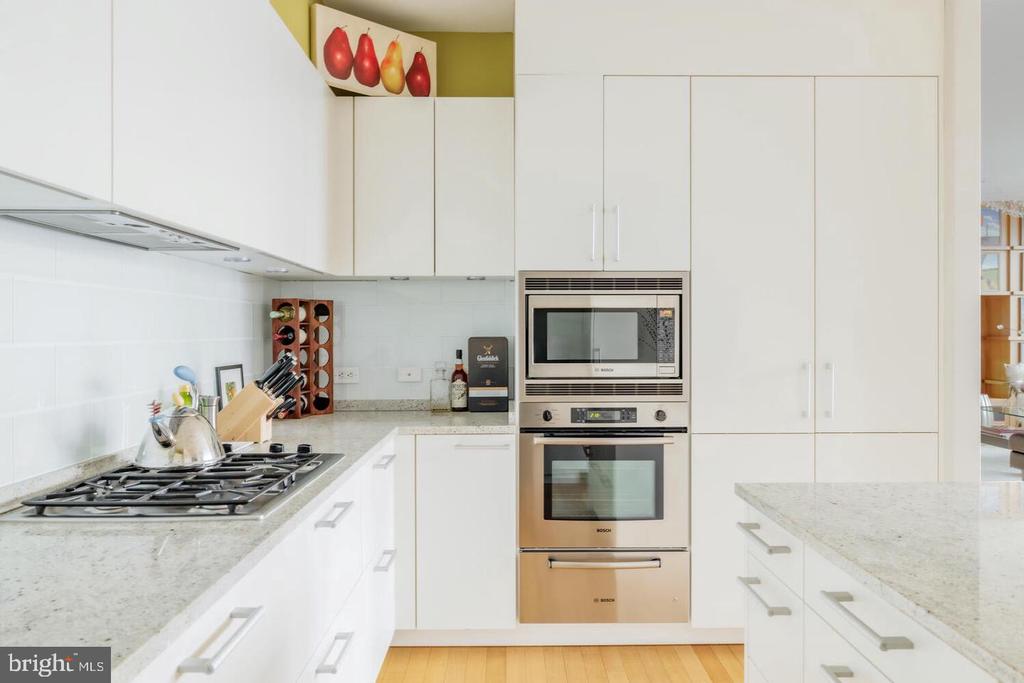 White kitchen with stone counters, gas cooktop, and built-in microwave and oven.
