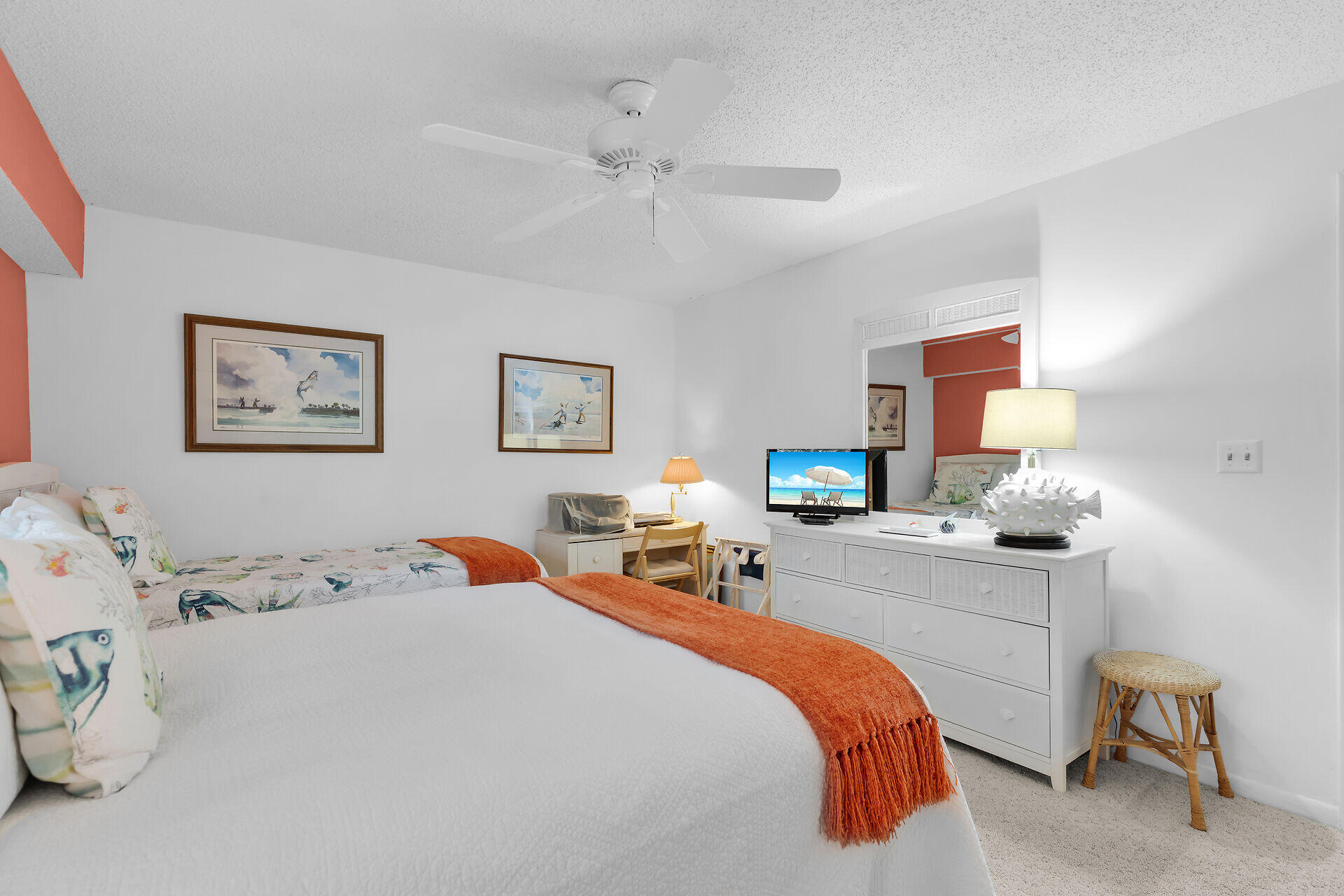 Furnished bedroom with twin beds, orange throws, tropical fish bedding, and coastal artwork.