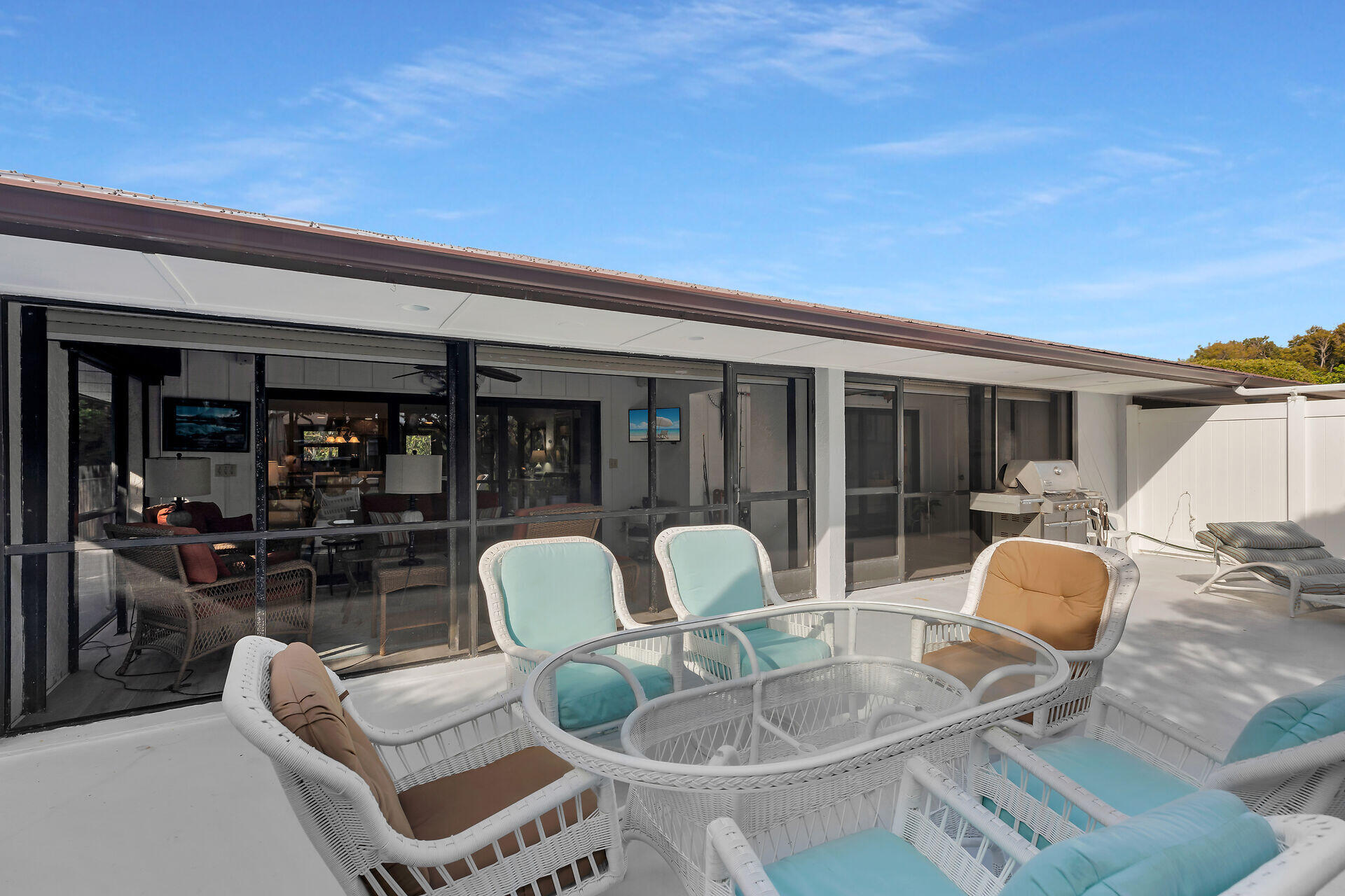 Furnished patio with white wicker seating, screened glass doors, and an outdoor grill.