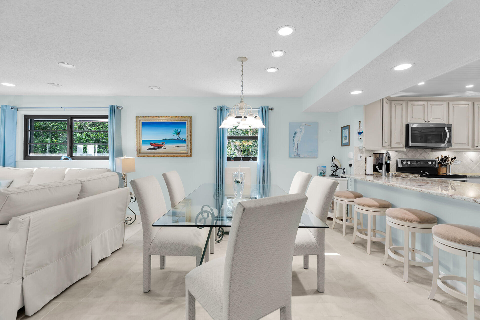 Open-plan dining area with glass table, white chairs, and a breakfast bar beside the living room.