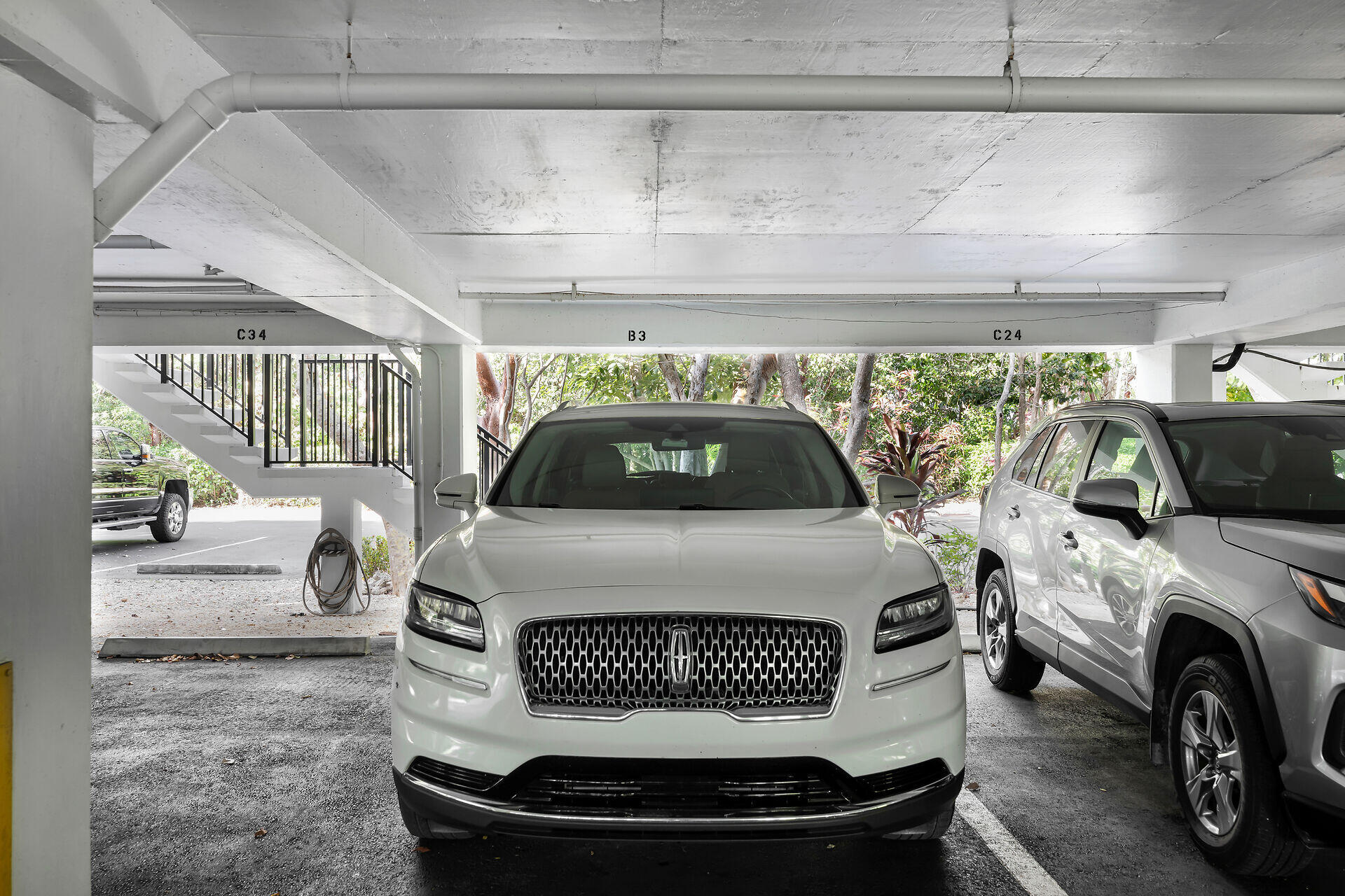 Covered parking area with a white SUV, adjacent parking spaces, and a staircase.