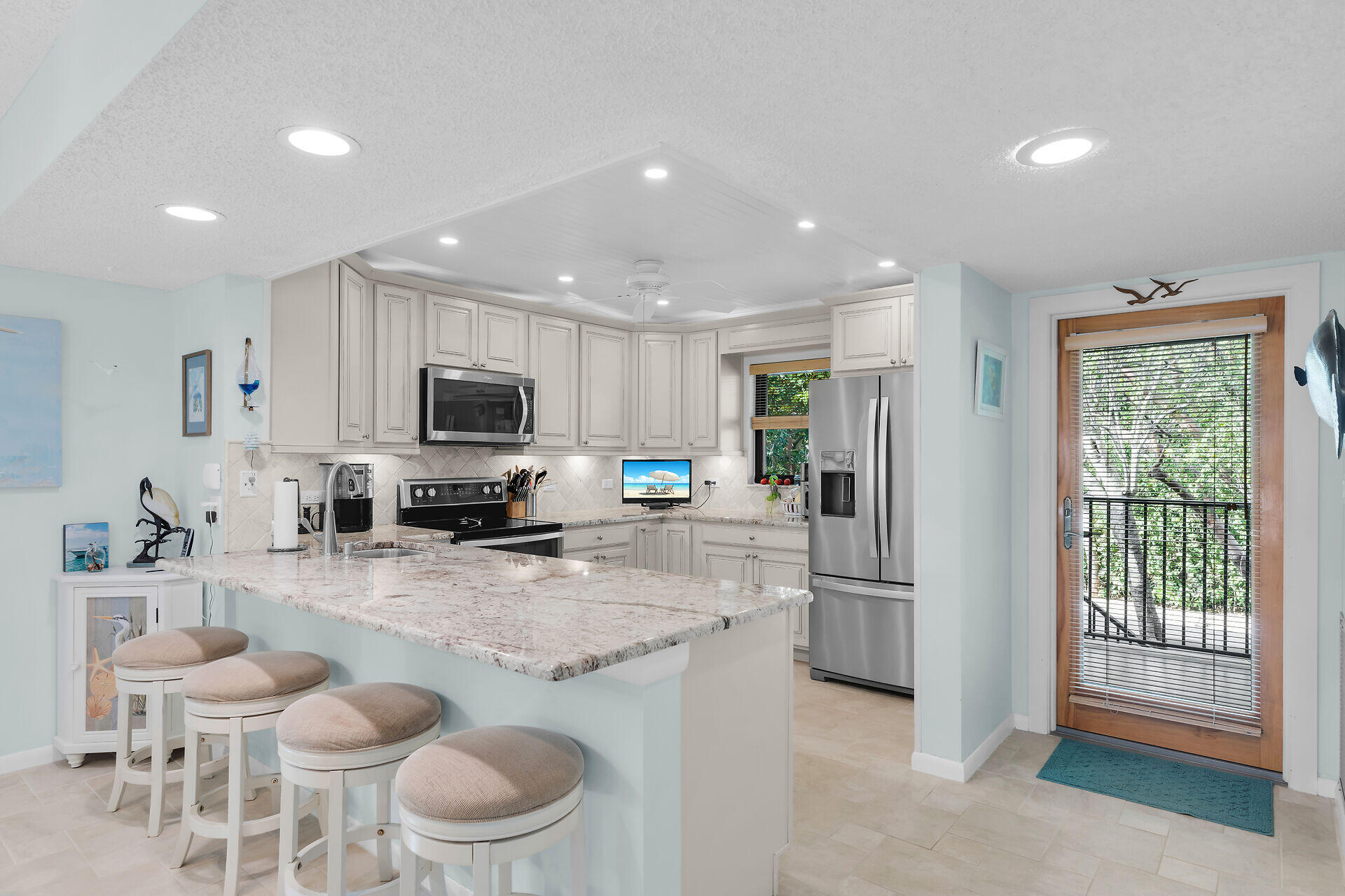 Kitchen with a large breakfast island, white cabinetry, stainless steel appliances, and a glass door overlooking greenery.