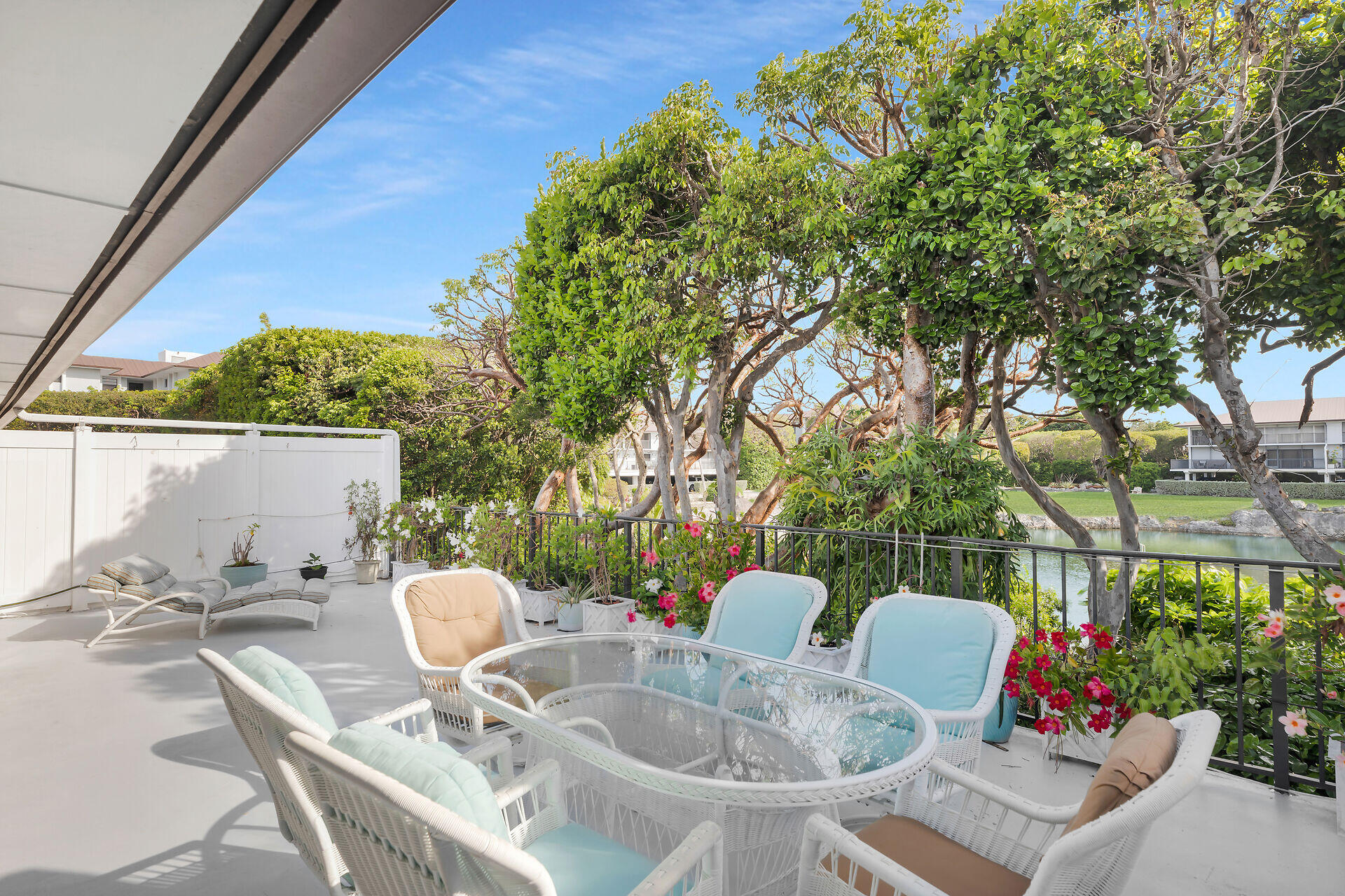 Waterfront patio with wicker seating and flowers overlooking a tree-lined canal