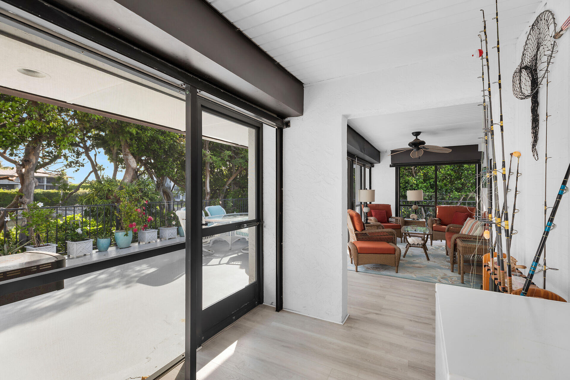 Covered screened patio with wicker seating, fishing rods, and garden views.