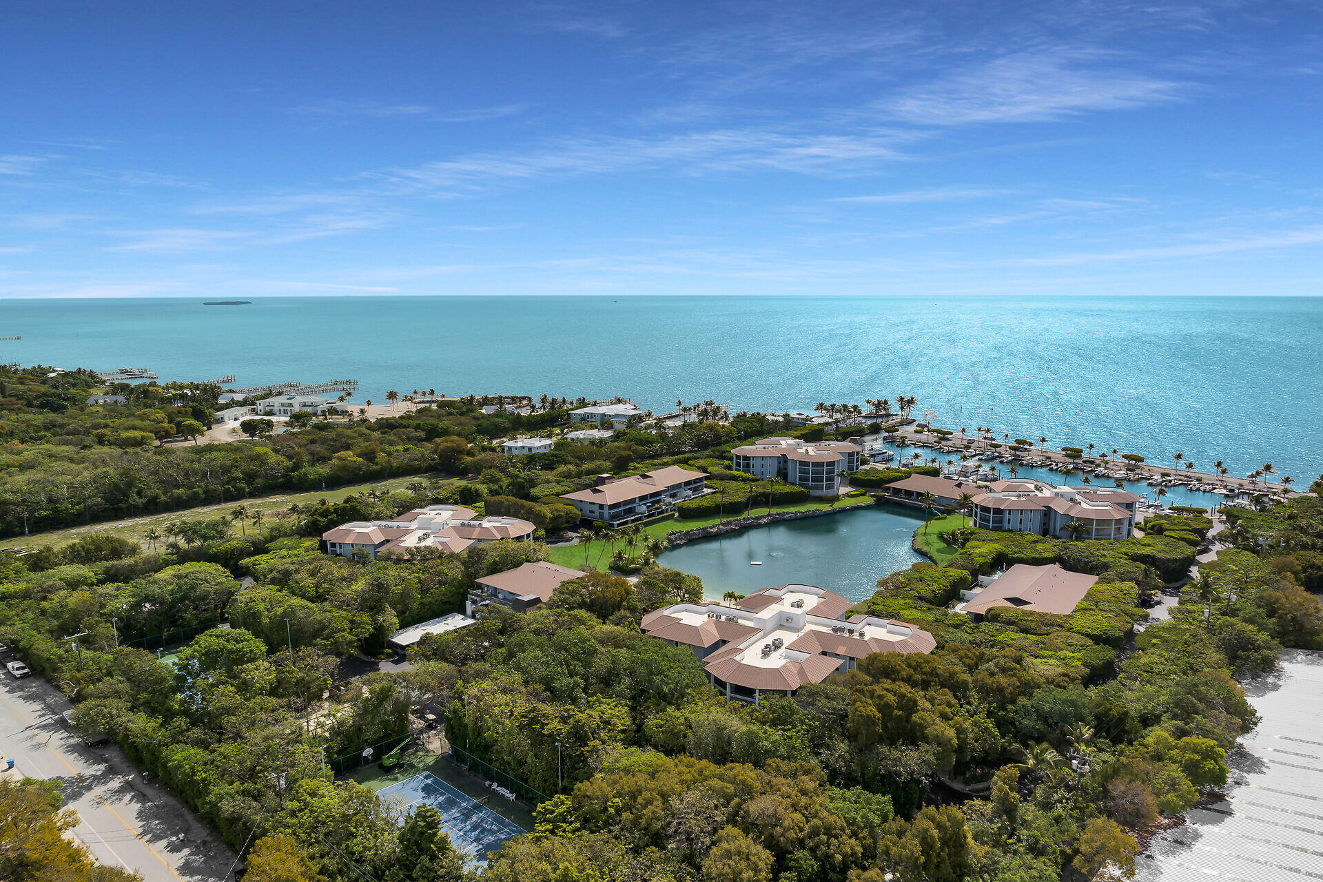 Aerial view of waterfront condominiums, a marina, and a lagoon beside the ocean.