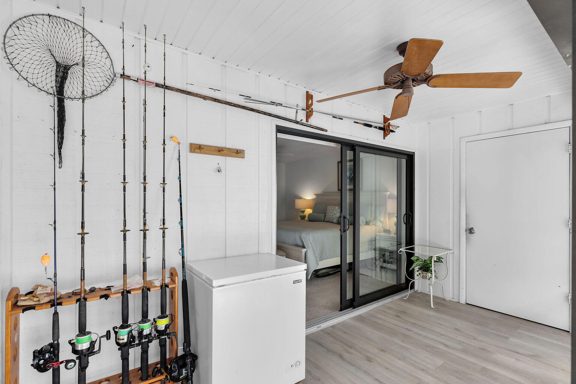 Covered porch with fishing gear, a chest freezer, and sliding glass doors to a bedroom.