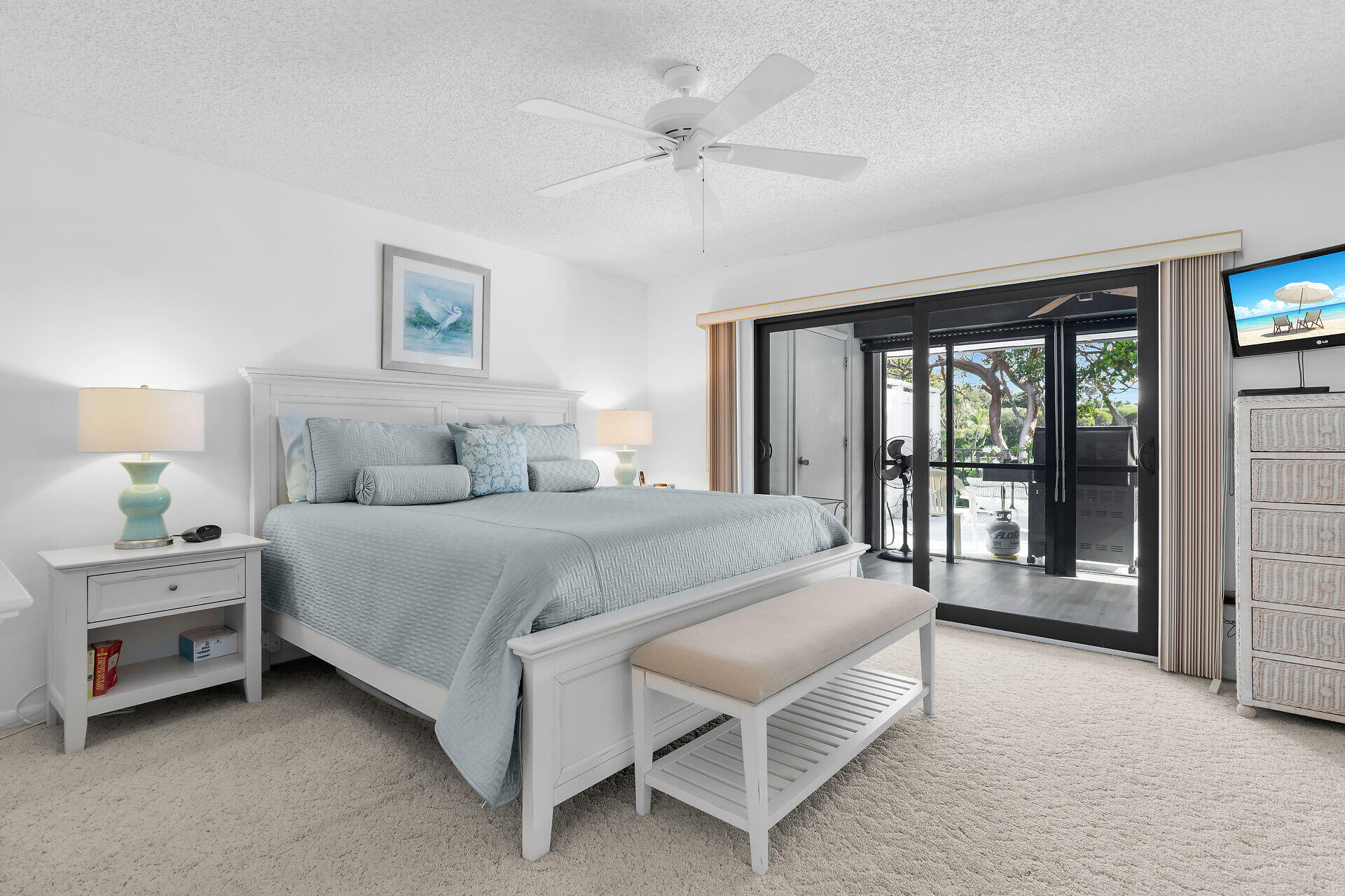 Bright bedroom with pale blue bedding and sliding glass doors opening to a covered patio.