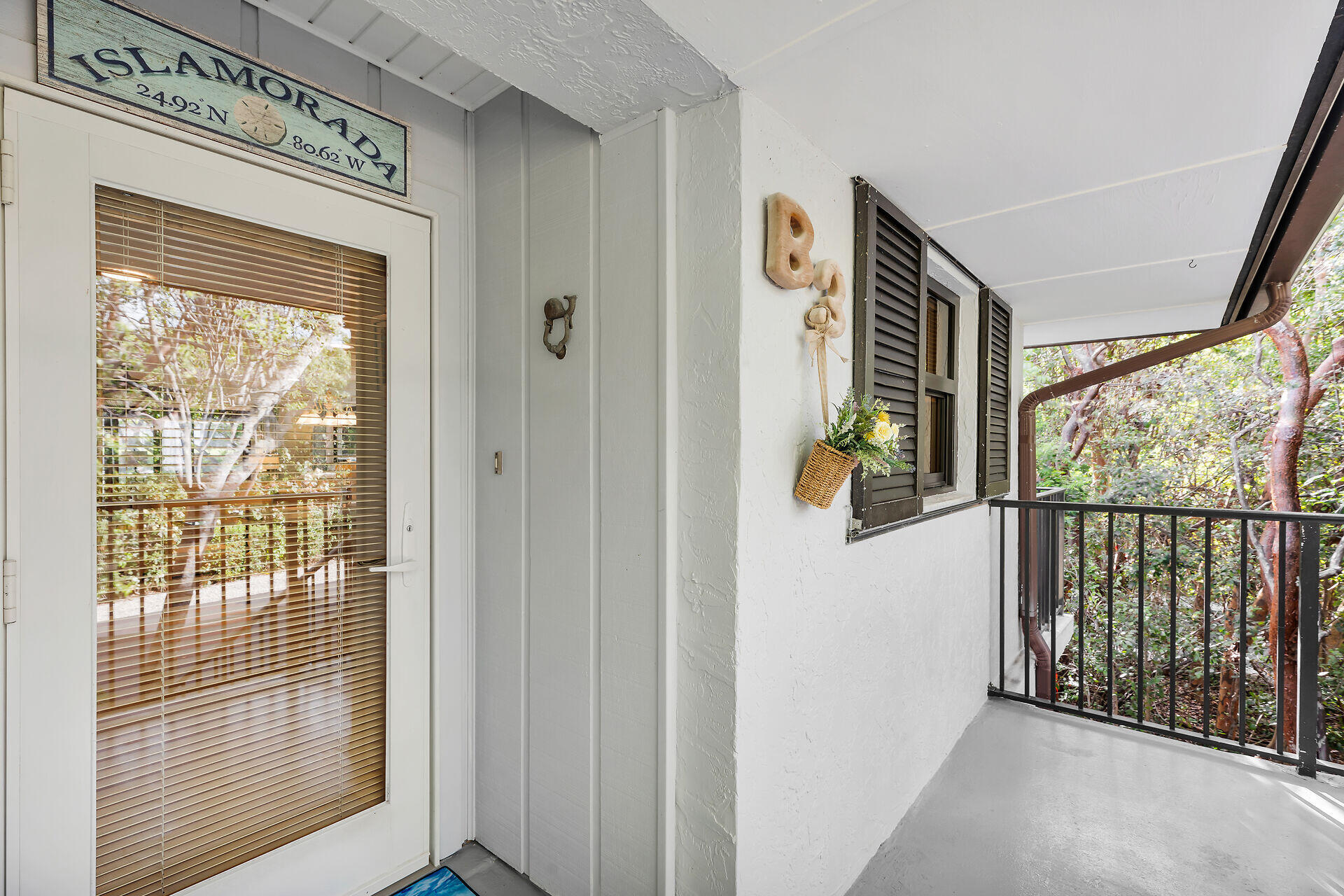 Covered entry with glass door and a balcony walkway overlooking tropical vegetation.