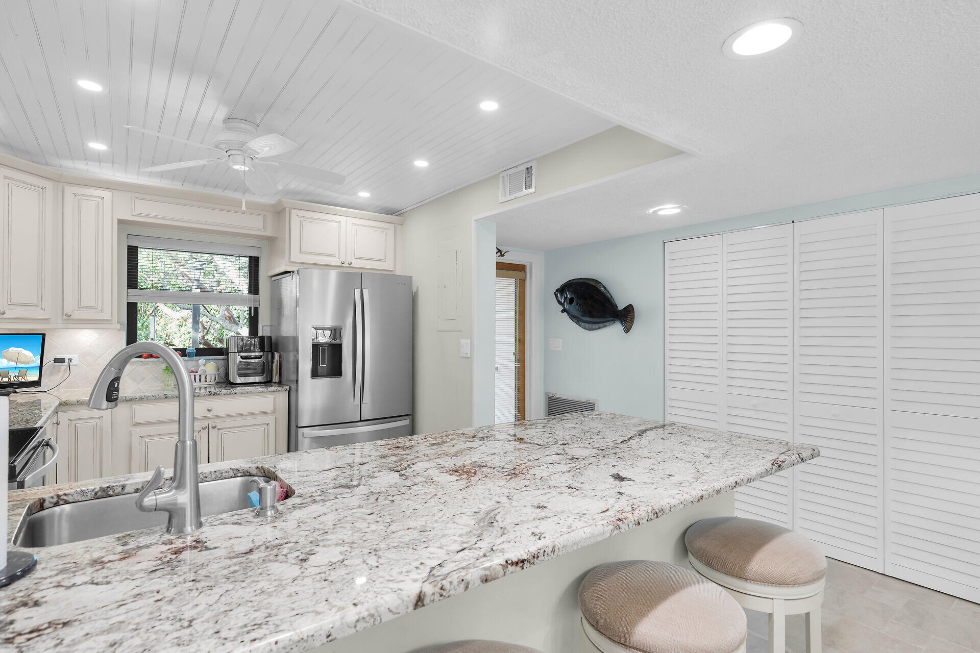 Kitchen with white cabinetry, stainless refrigerator, and a large granite island with sink and seating.