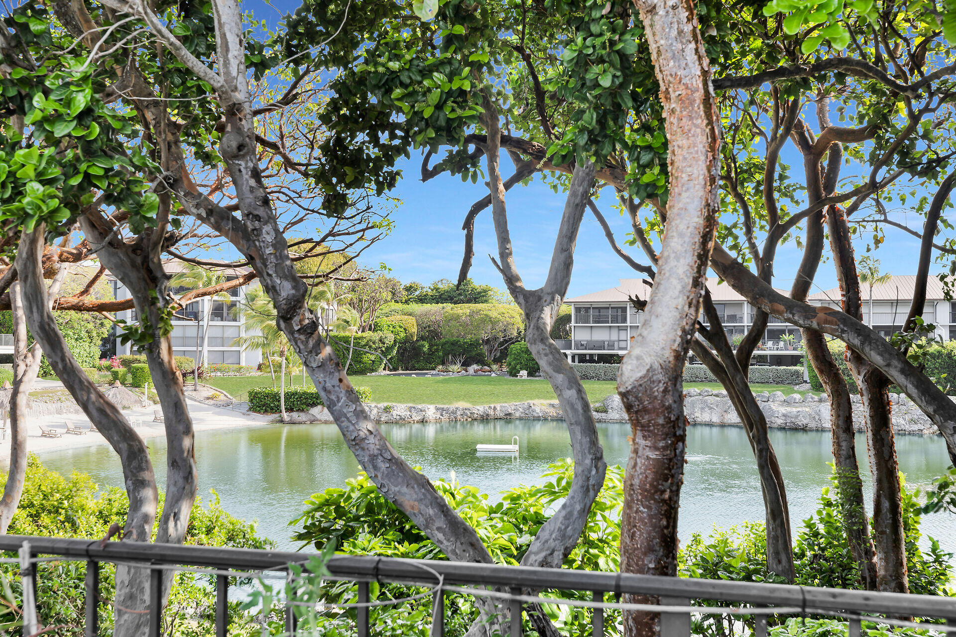 Waterfront condominium grounds with a calm lagoon, floating dock, and leafy trees.