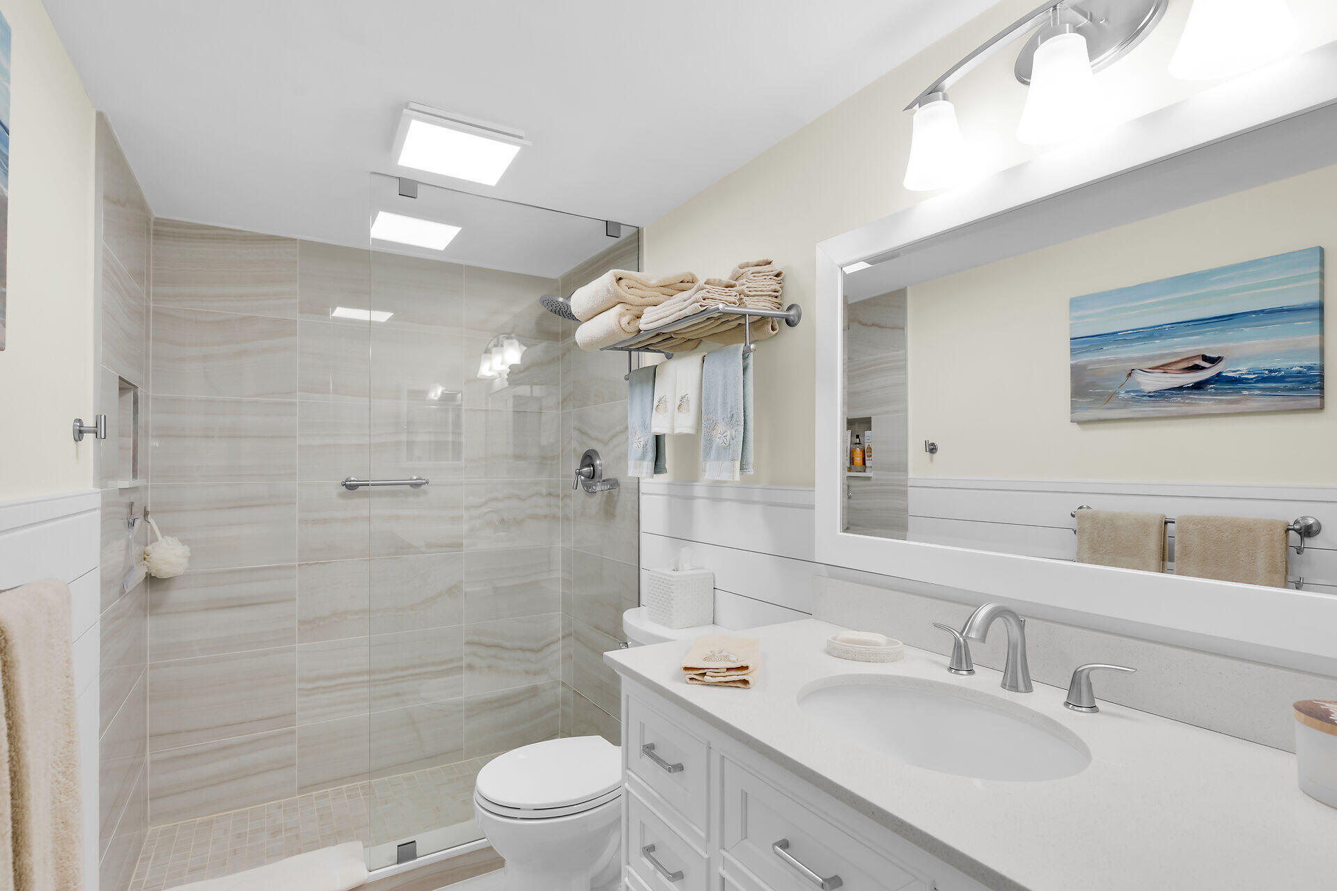 Bathroom with a glass walk-in shower, pale tile, and white vanity.