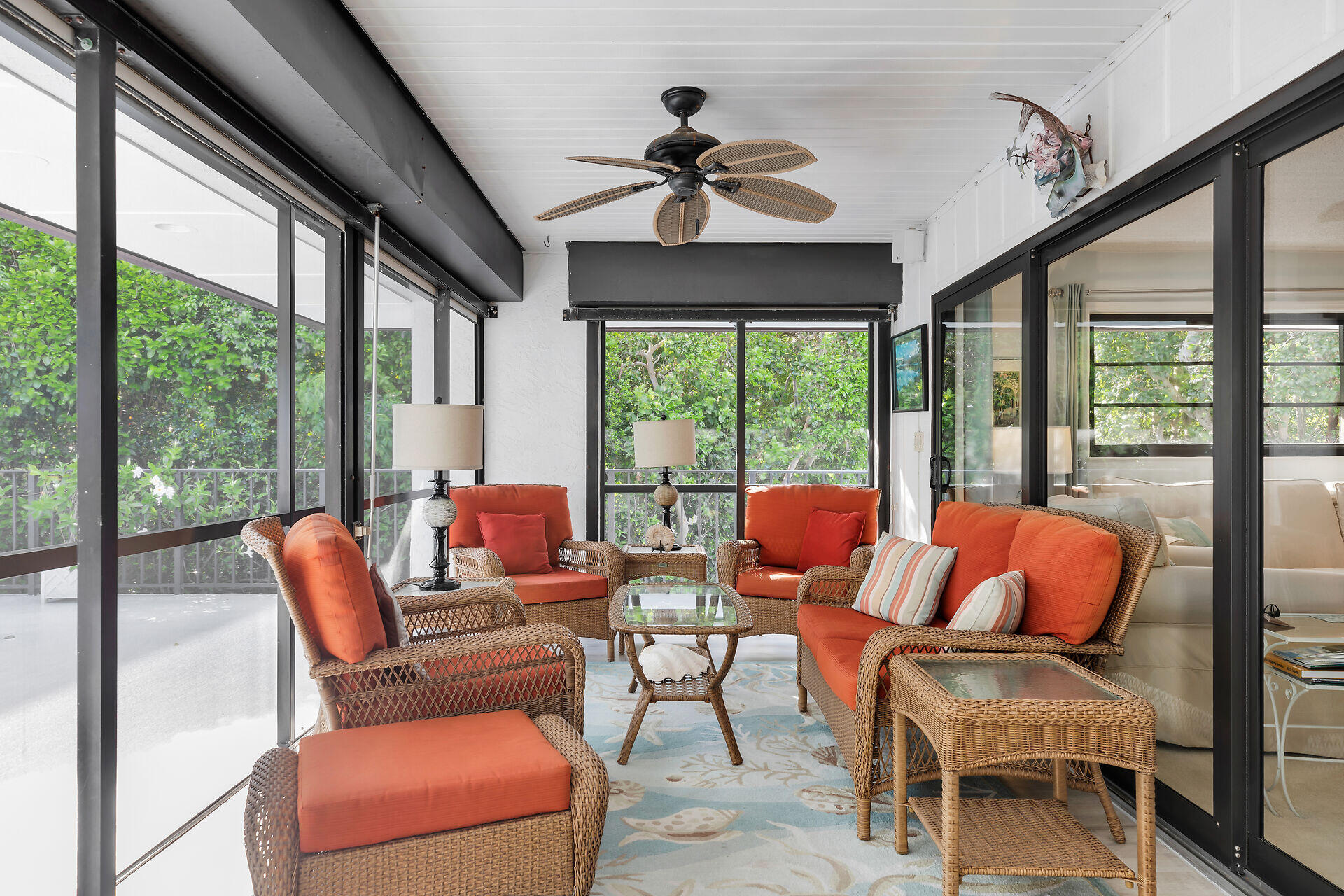 Screened porch with orange-cushioned wicker seating and views of lush greenery.